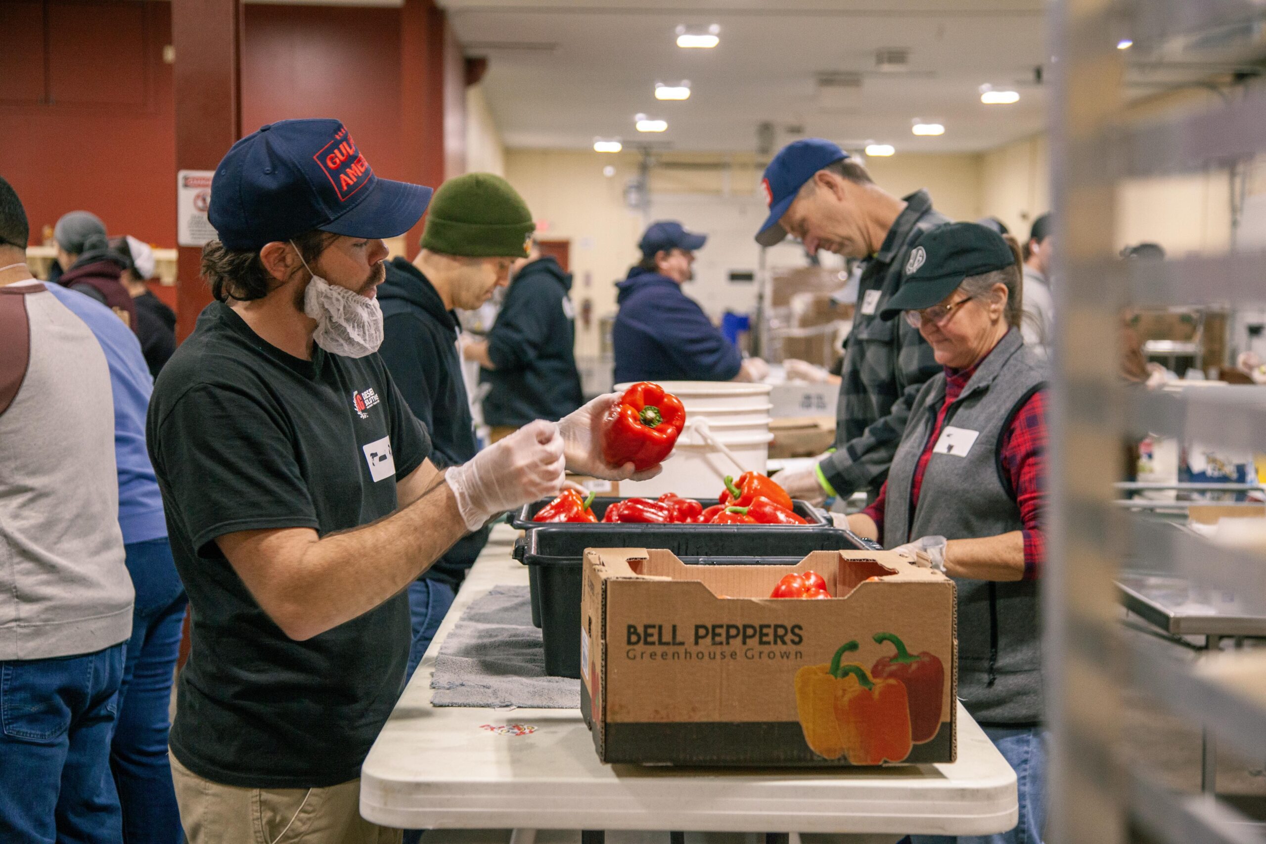 Volunteers sorting and packing red bell peppers in a food distribution center, focused on efficient food preparation and community support.