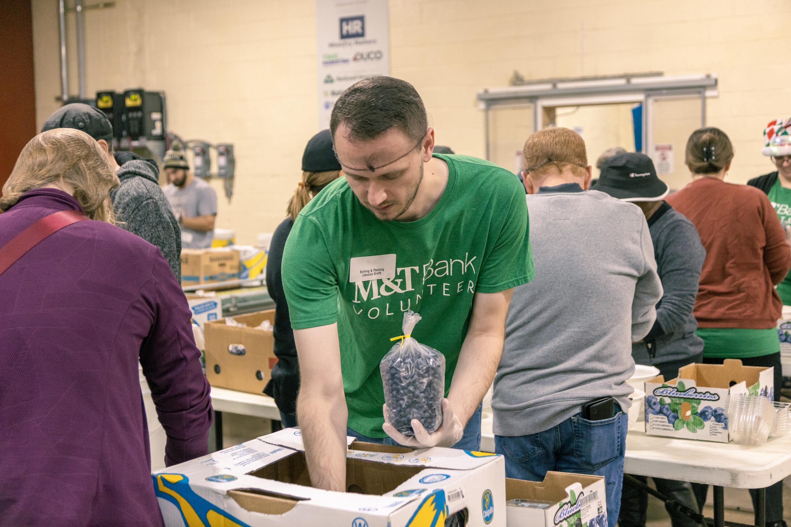 Volunteers sorting and packing food items at a community service event, with a focus on teamwork and collaboration in a warehouse setting.