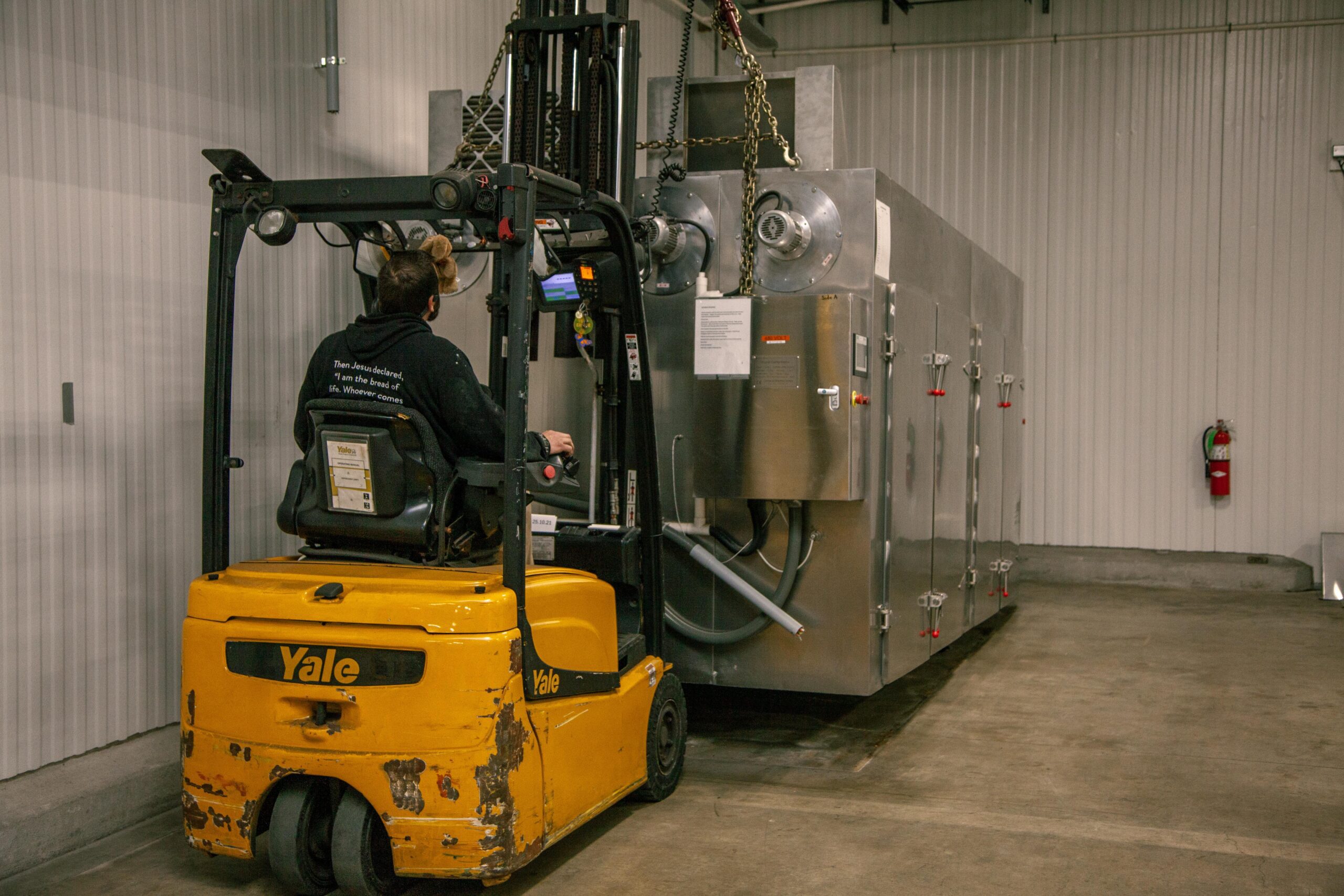 A forklift operator maneuvering a Yale forklift to transport a large industrial oven in a warehouse setting, showcasing efficient material handling in a commercial environment.