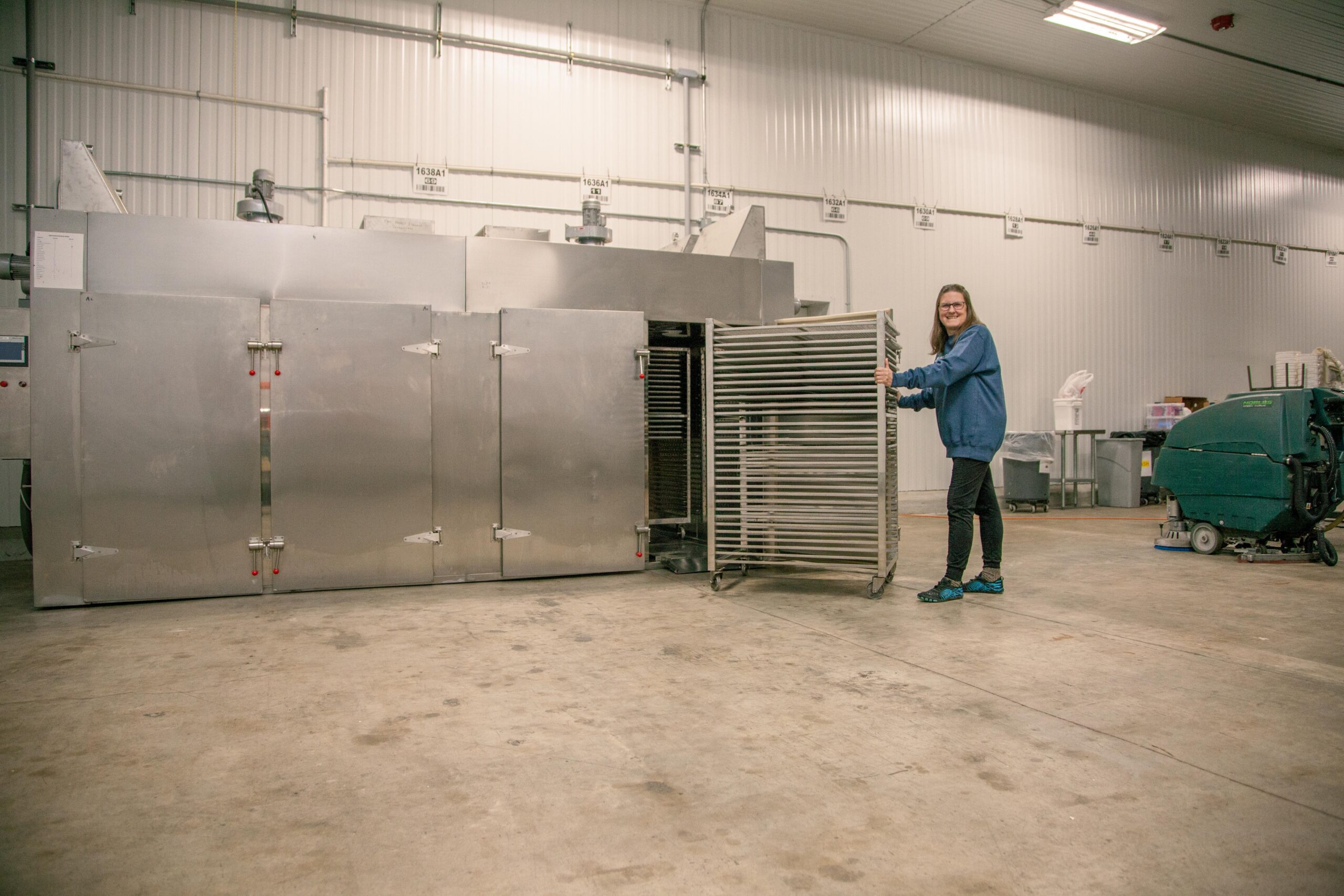 Woman operating a commercial stainless steel oven in a spacious industrial kitchen, showcasing food preparation equipment and a clean work environment.