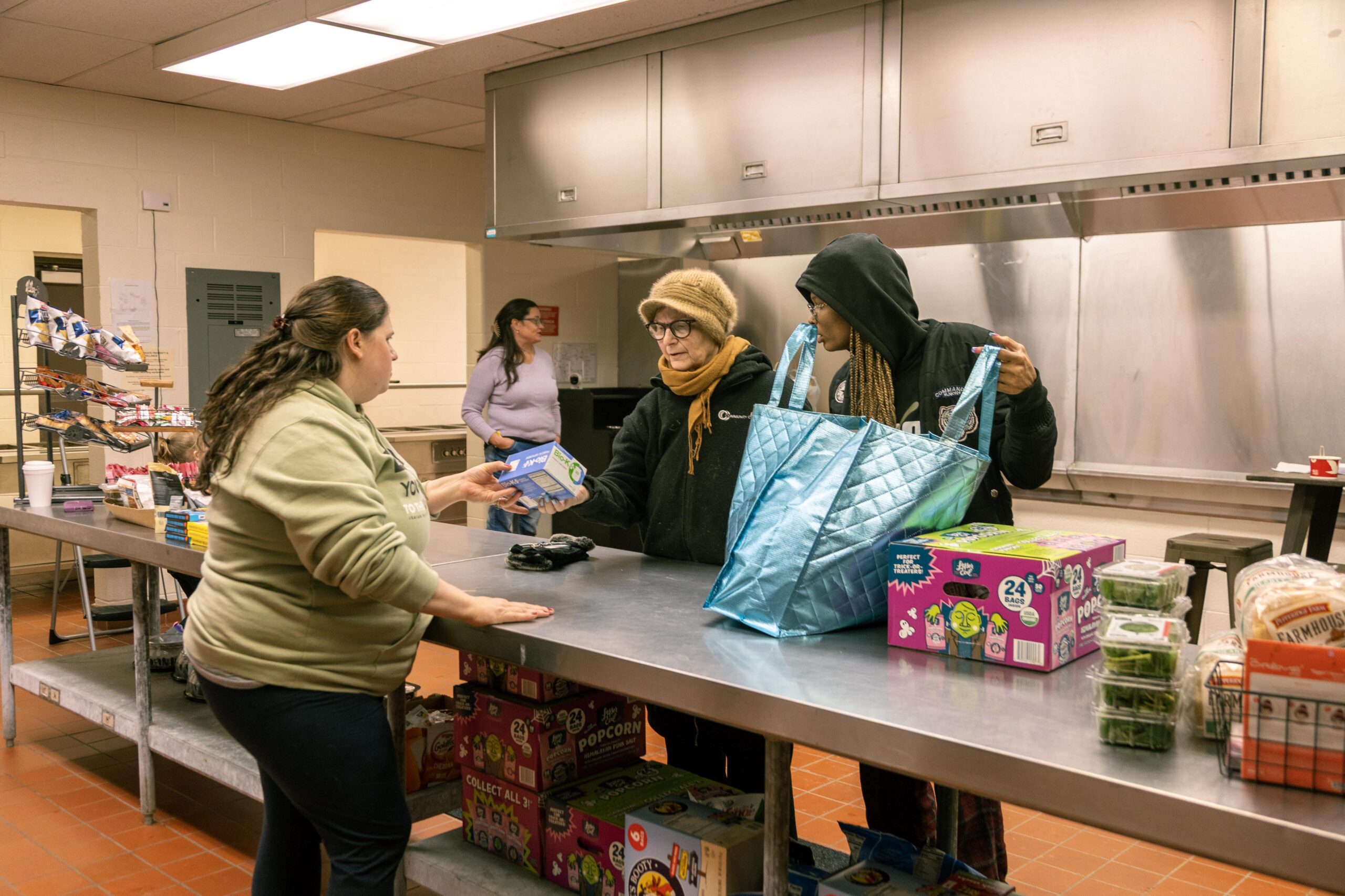Community members receiving food assistance at a local food pantry, showcasing an indoor kitchen setting with staff and clients interacting at a service counter.