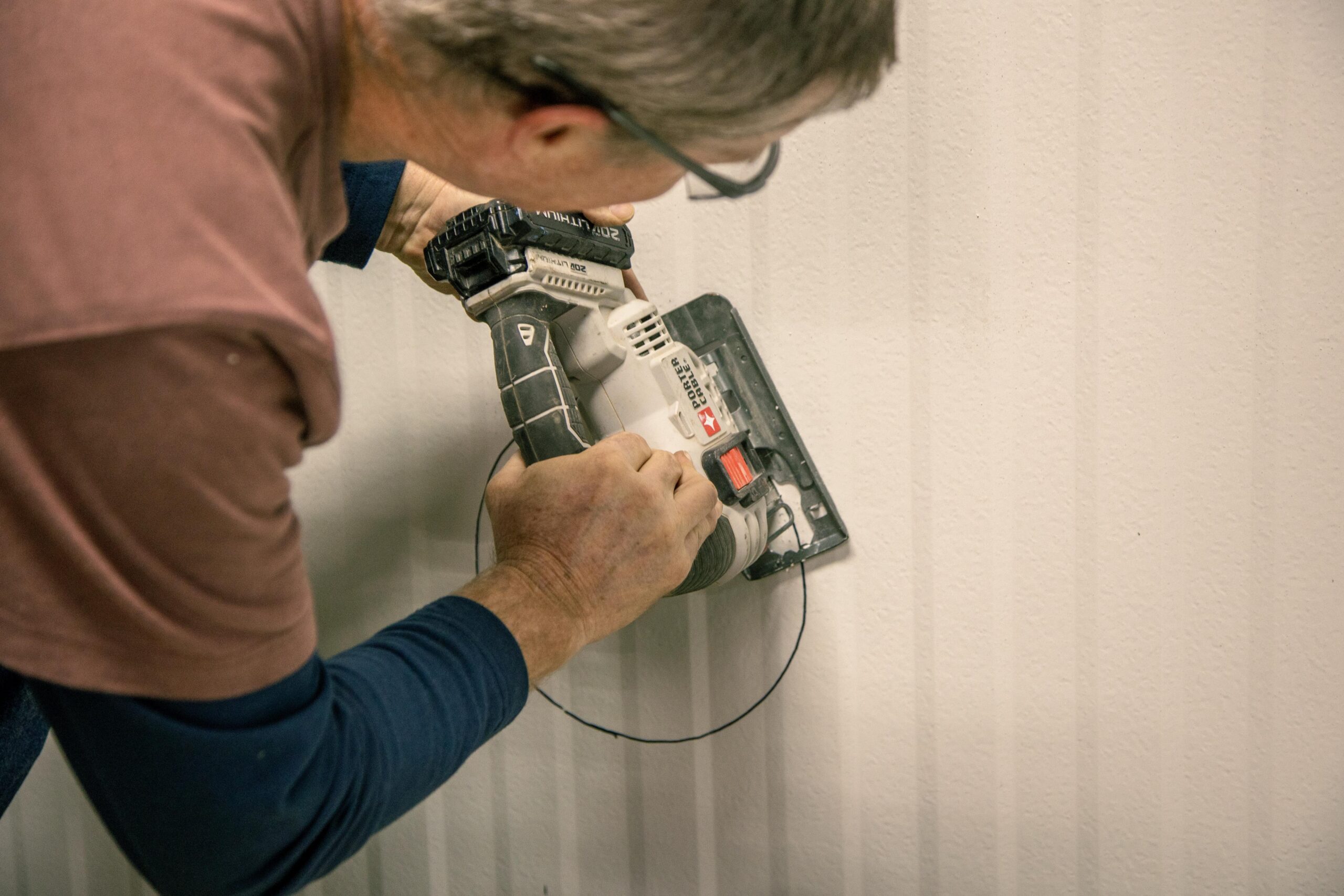 A person using a circular saw to cut a circular opening in a textured wall, demonstrating home improvement techniques and woodworking skills.