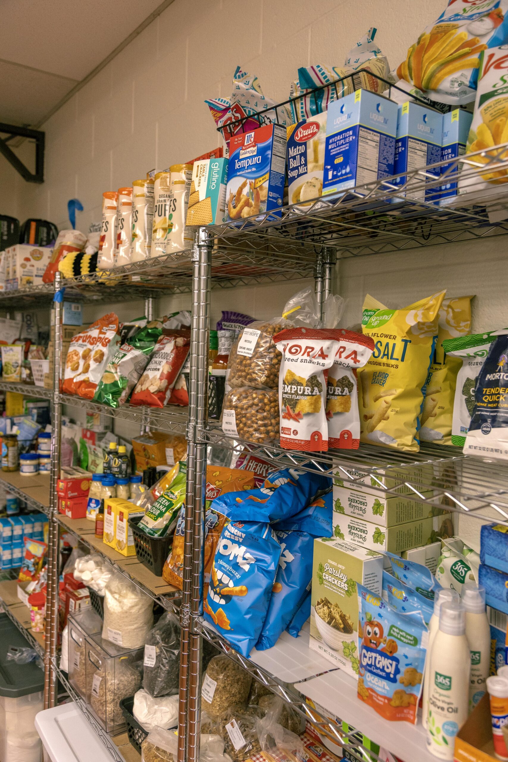 Shelves stocked with various food items including snacks, baking supplies, and pantry essentials, showcasing a diverse selection of brands and products in a well-organized storage area.