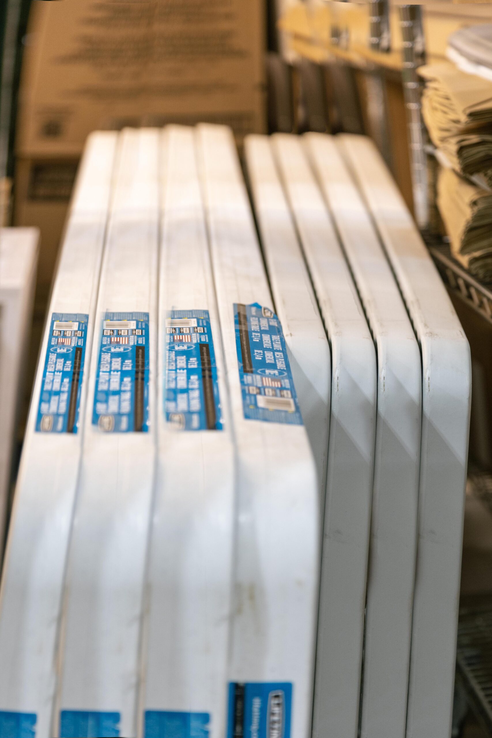 Stack of white, insulated window frames with blue labels, stored in a warehouse setting. The image showcases multiple frames lined up, emphasizing their design and packaging, suitable for home improvement projects.