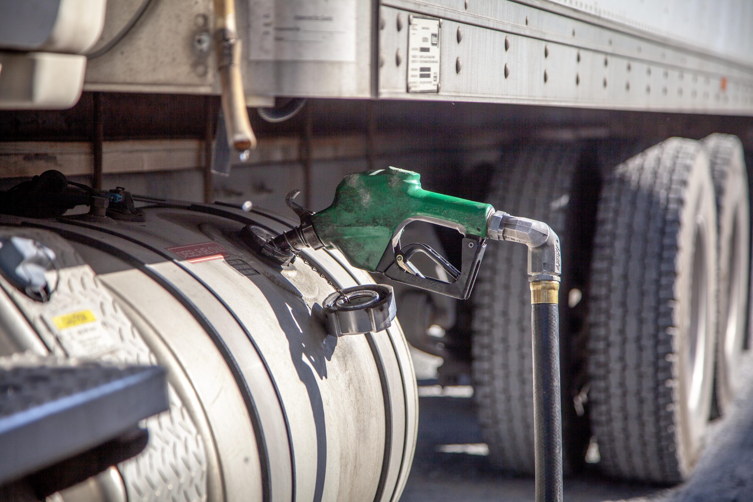 Fuel nozzle inserted into a truck's fuel tank, highlighting the refueling process for commercial vehicles. The image showcases the truck's metallic tank and surrounding wheels, emphasizing the importance of fuel management in transportation.