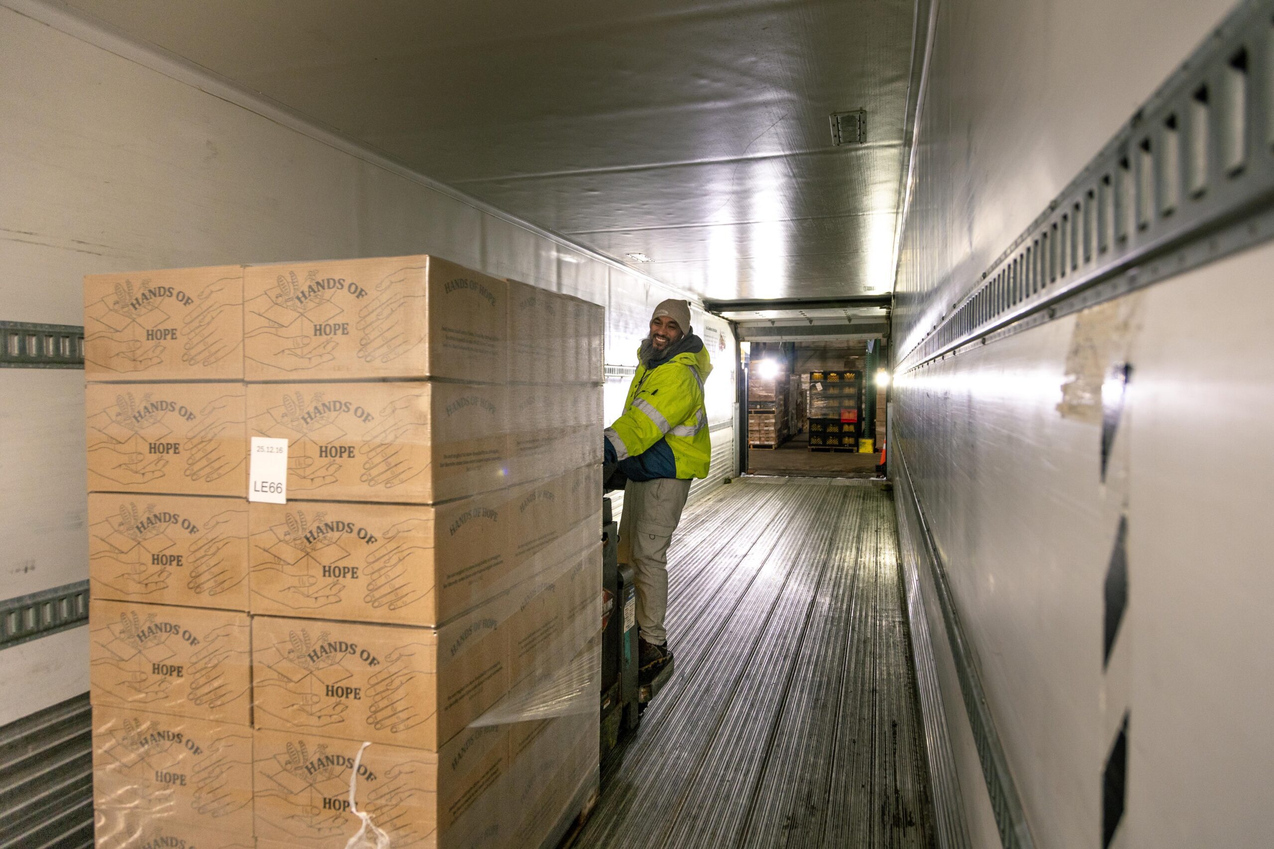 Worker unloading boxes labeled "Hands of Hope" from a trailer in a warehouse, showcasing logistics and community support efforts.