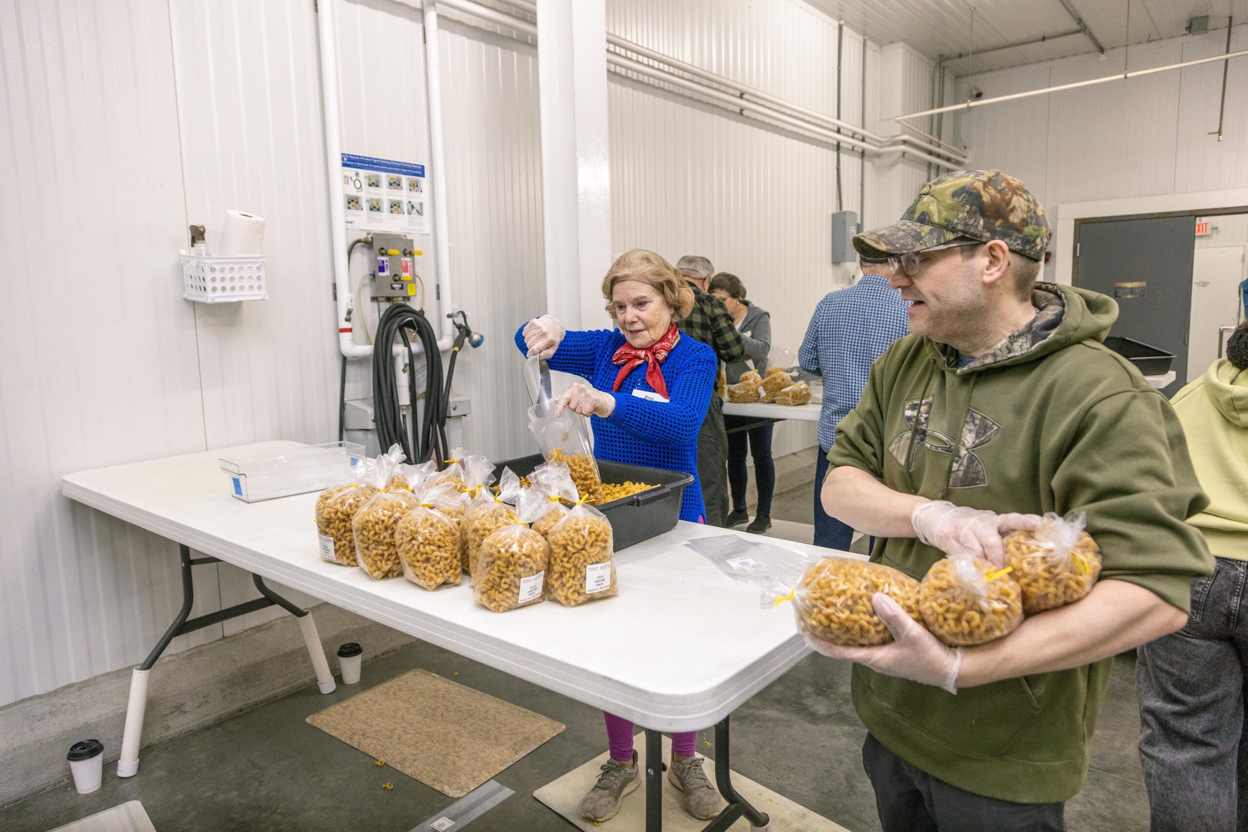 Volunteers packaging pasta in a food processing facility, showcasing teamwork and community involvement in food distribution efforts.