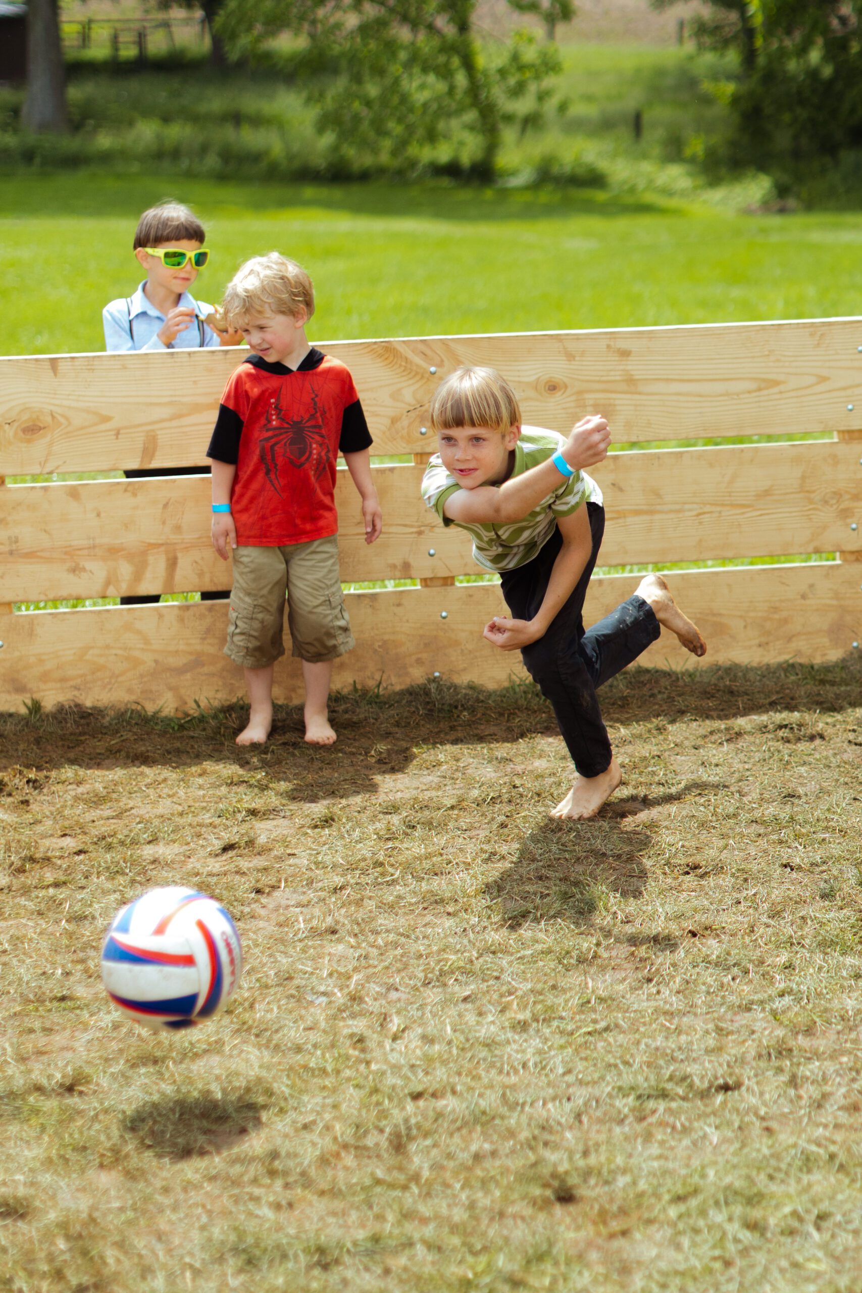 Children playing soccer in a grassy area, with one child kicking a ball while two others watch. The scene captures a fun outdoor activity, showcasing the joy of youth and sportsmanship.