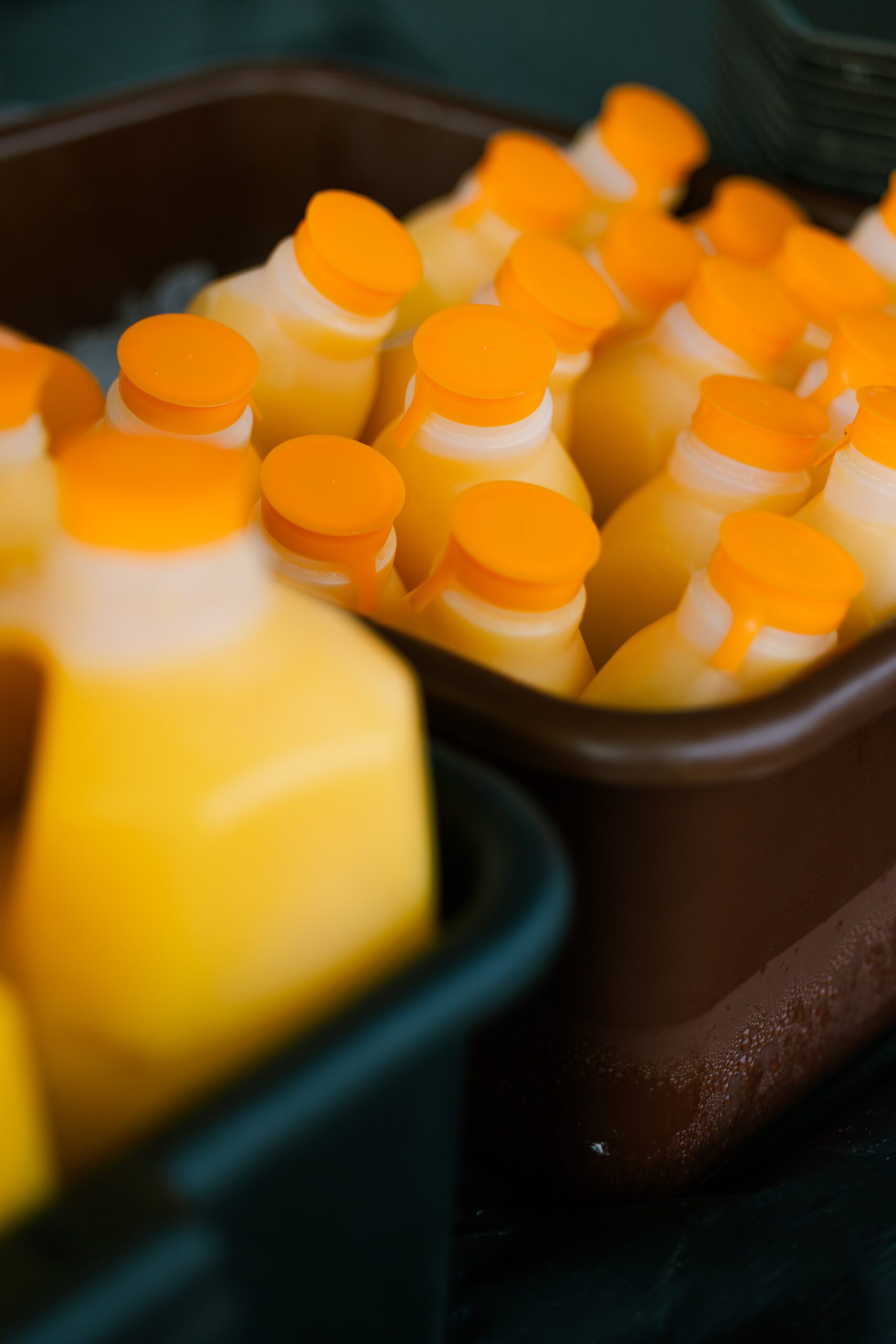 Bottles of fresh orange juice with bright orange caps arranged in a container, showcasing a vibrant and appealing display of beverages.