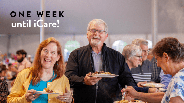 Group of people enjoying a meal at a community event with a banner stating "One Week until iCare!" in a festive tent setting.